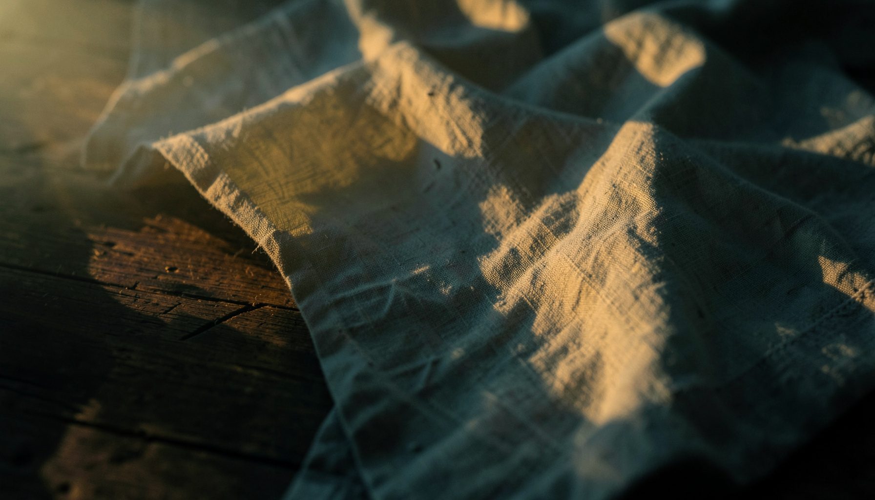 Linen cloth draped over a wooden surface, illuminated by warm sunset light creating gentle shadows.